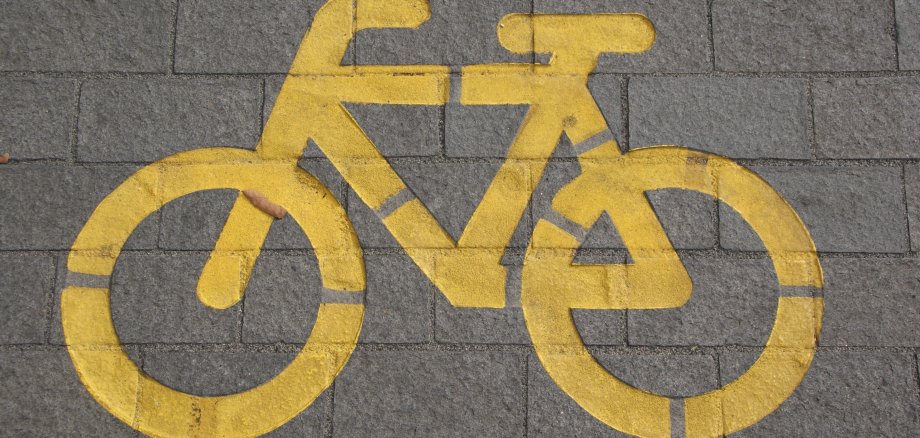 Ein gelbes Fahrrad Symbol wurde auf einen gepflasterten Boden gemalt. Es signalisiert einen Fahrradweg.