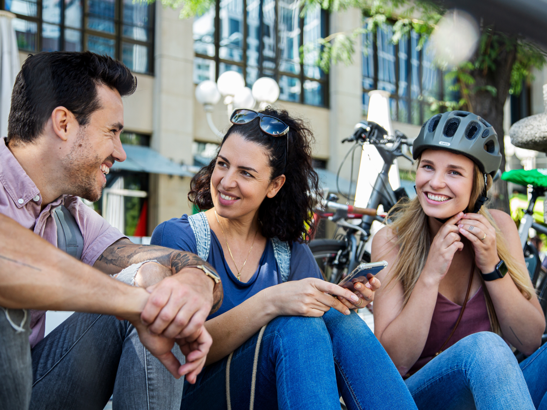 links ein Mann, recht zwei Frauen, sitzen zusammen mit Fahrradhelm und Fahrrad im Hintergrund