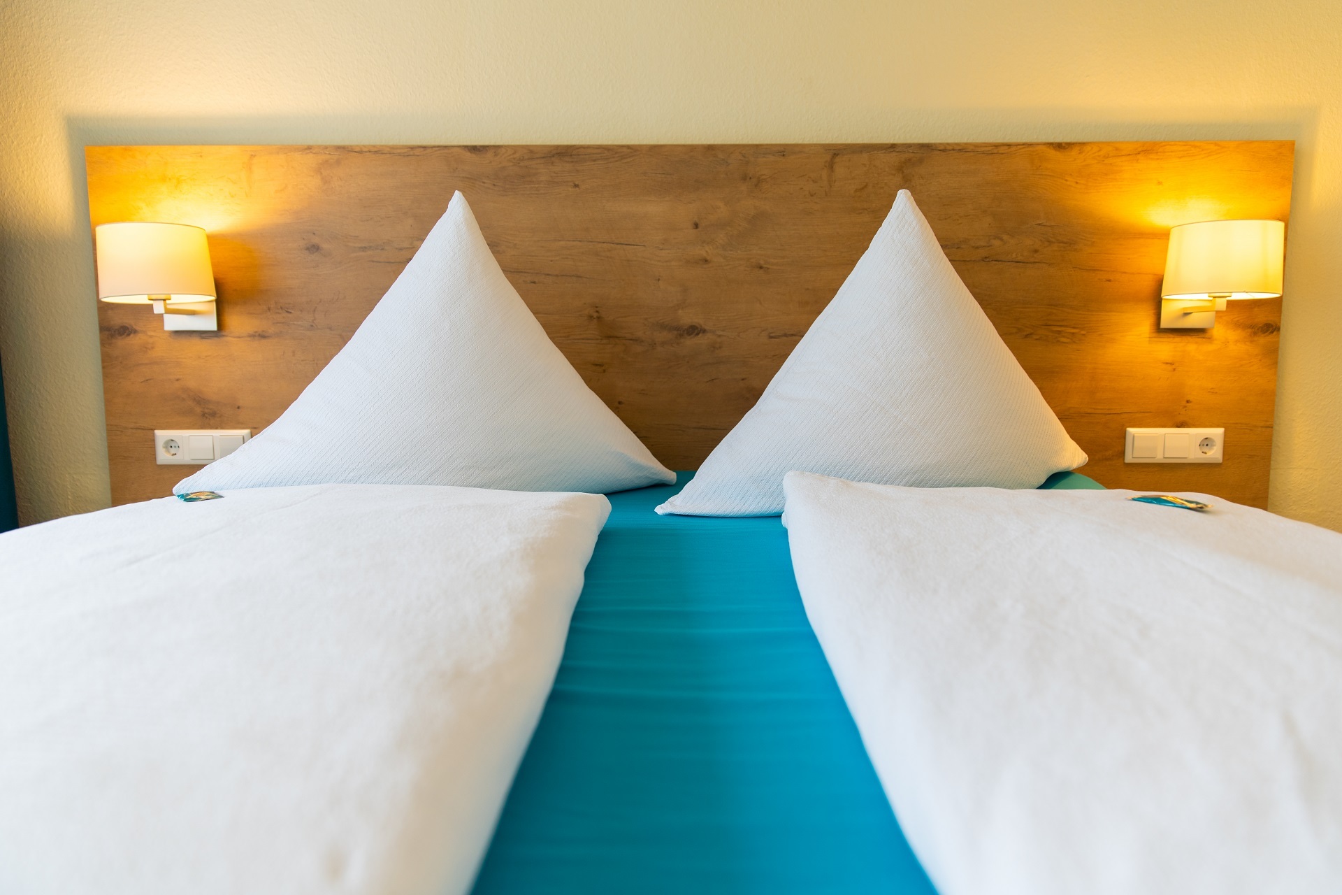 Zu sehen ist ein Doppelbett mit blauem Laken und schön drapierten Decken und Kopfkissen