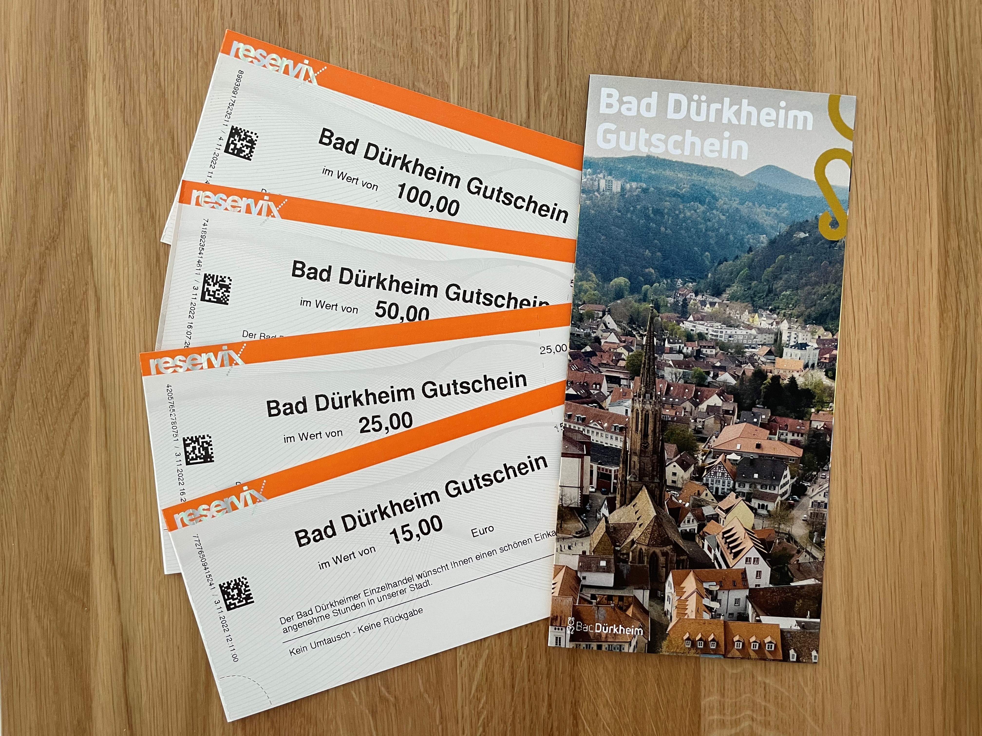 Zu sehen sind aufgefächert vier Bad Dürkheim Gutscheine in den Preiskategorien 15€, 25€, 50€ und 100€. Daneben der Gutscheinflyer von vorne.
