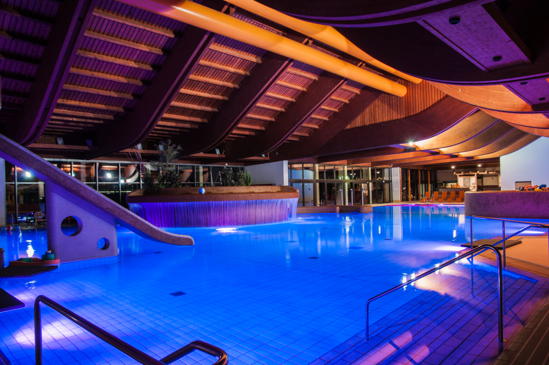 Das Innenbecken des Erlebnisbads Salinarium ist blau angestrahlt. Zu erkennen ist das Nichtschwimmerbecken, den Whirlpool und eine steinerne Rutsche.