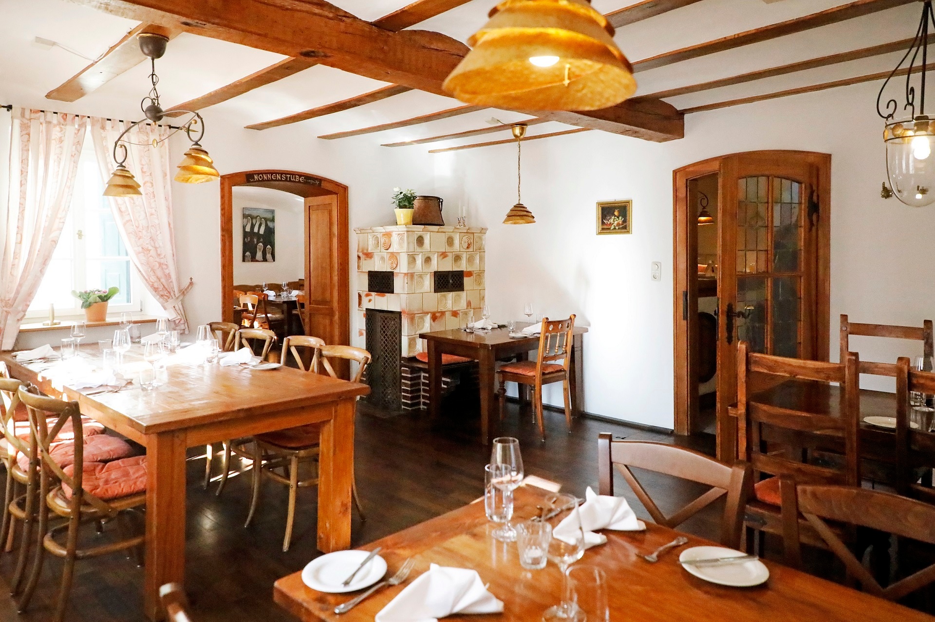 Der gemütliche urige Innenbereich des Restaurant Käsbüro. Im Hintergrund zwischen den Tischen befindet sich ein alter Kachelofen. links und rechts zwei Türen.