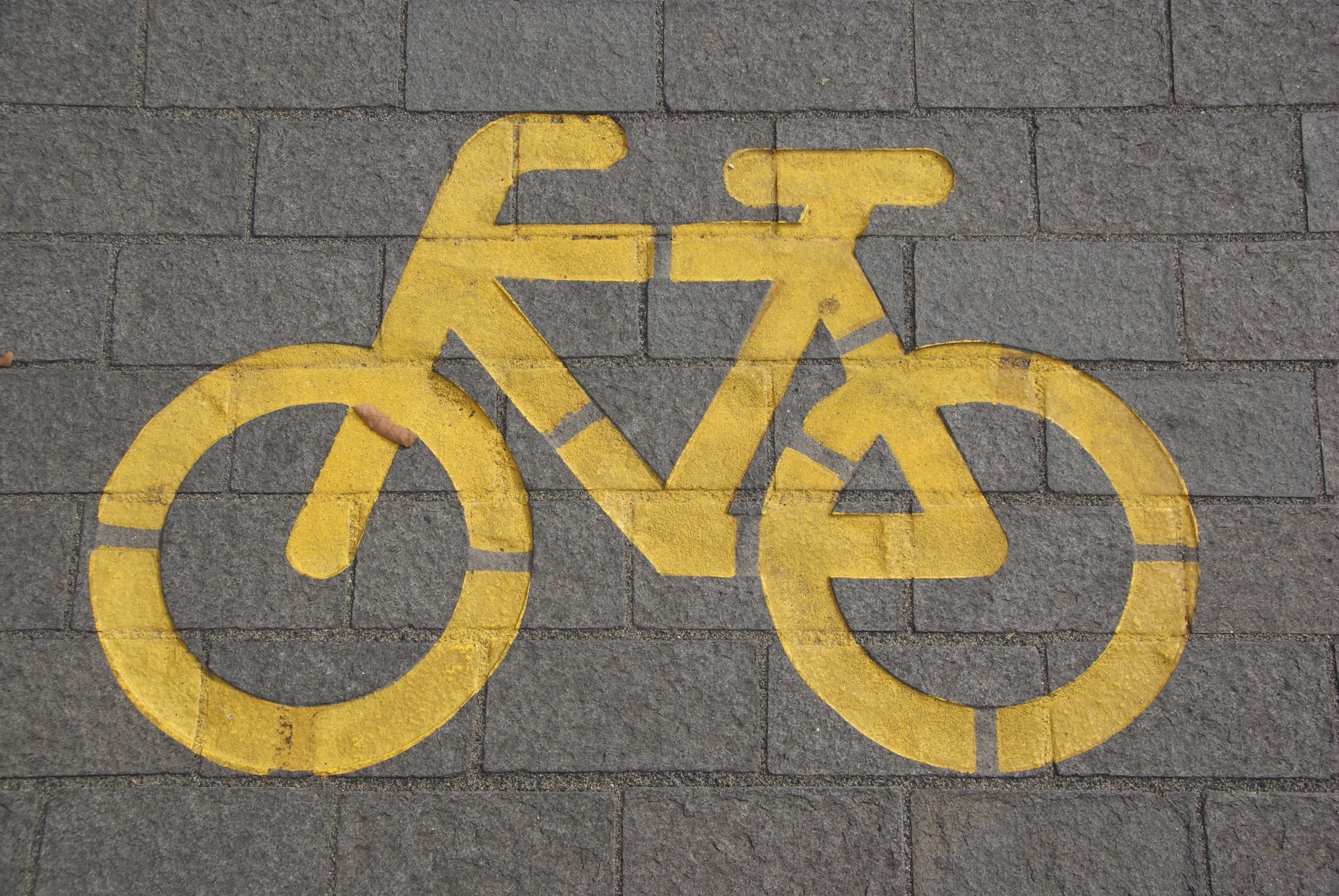Ein gelbes Fahrrad Symbol wurde auf einen gepflasterten Boden gemalt. Es signalisiert einen Fahrradweg.