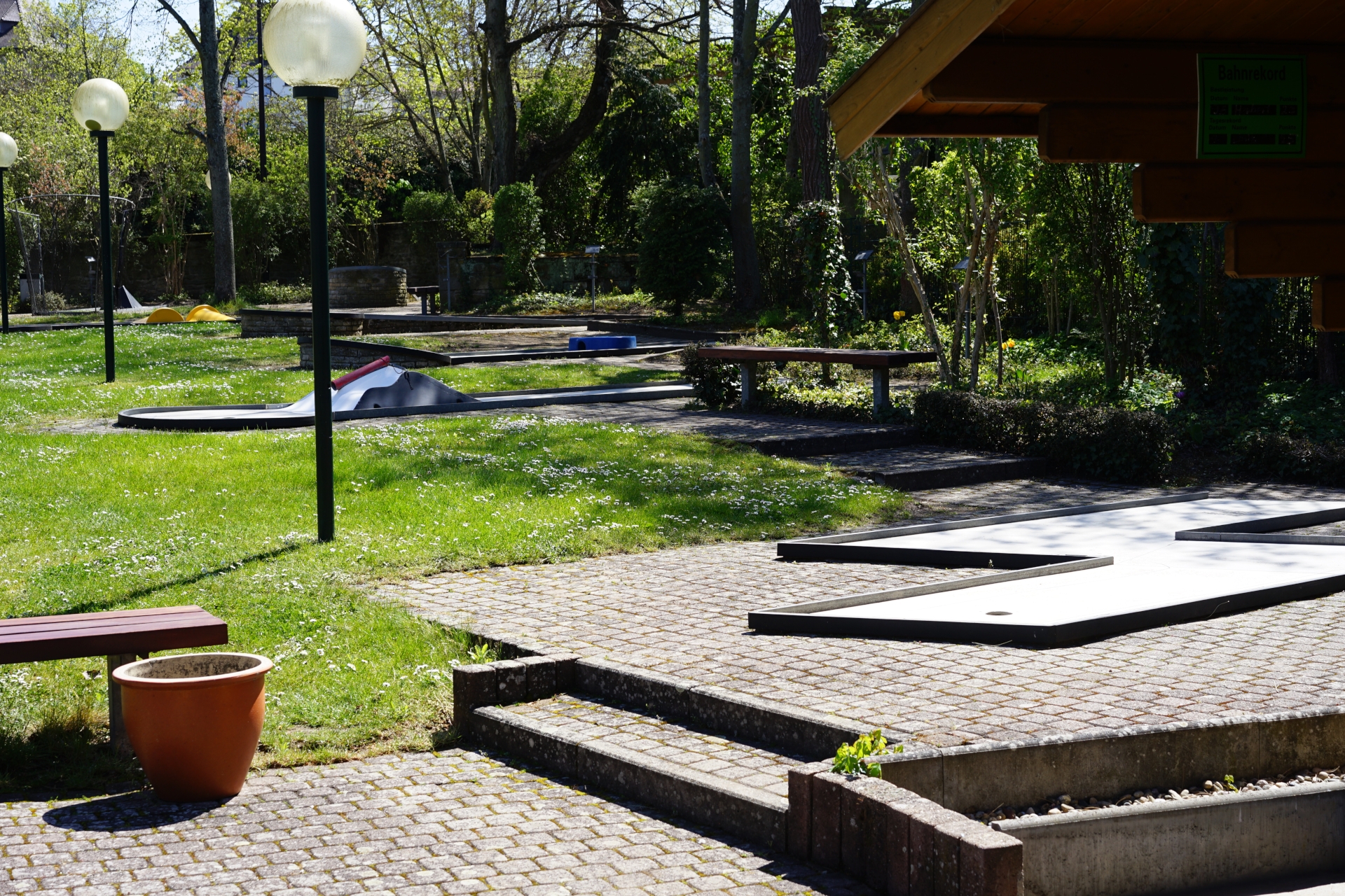 Minigolfplatz Bad Dürkheim Der Eingangsbereich mit den ersten Minigolfbahnen die von Bäumen bzw. Schatten umgeben sind.