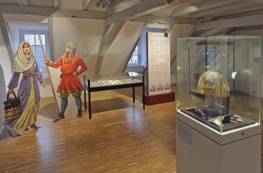 Blick in einen Ausstellungsraum mit Exponaten aus der keltischen und fränkischen Periode, im Vordergrund ein goldener Helm.
