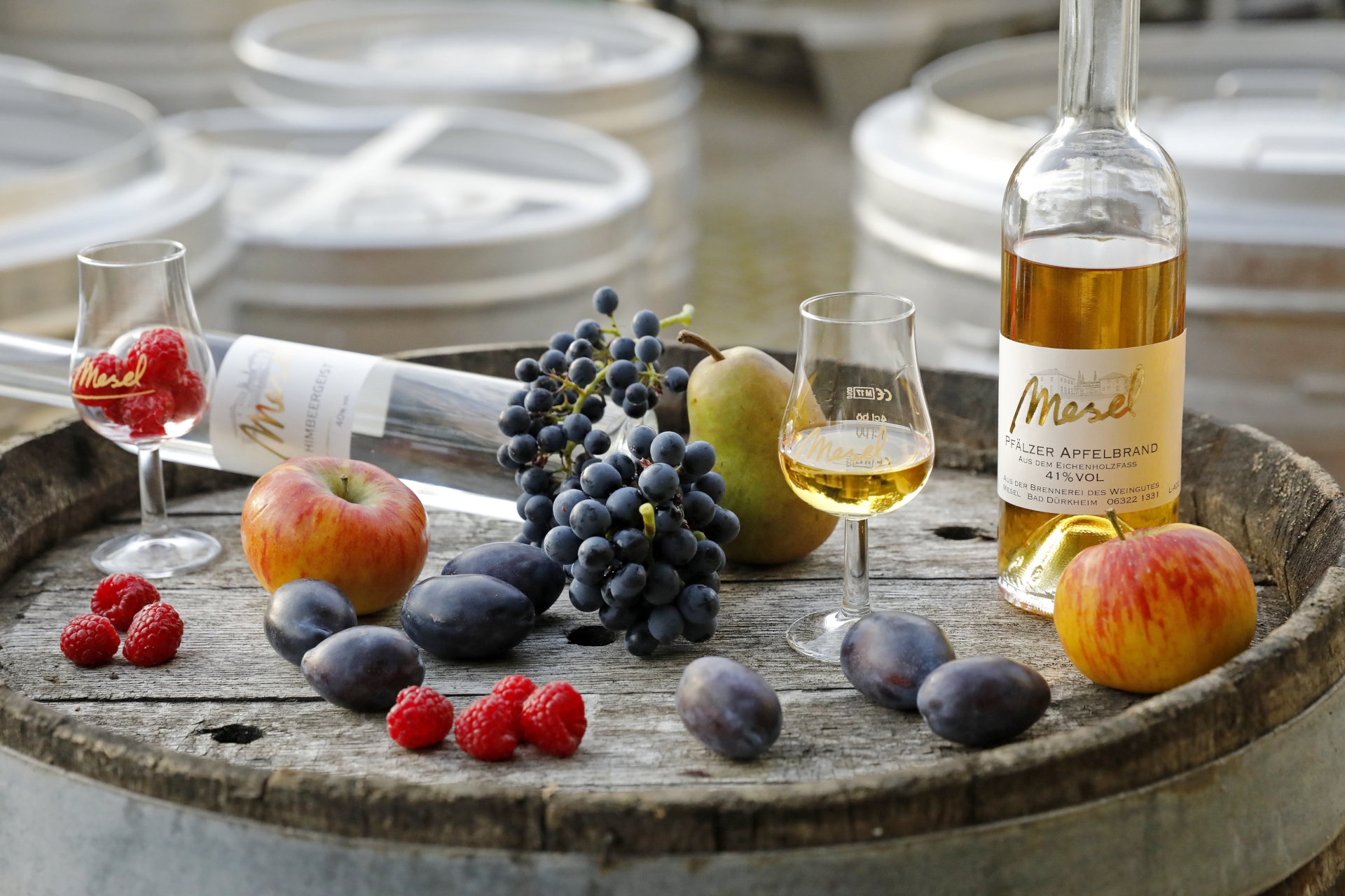 Brände mit Obst vom Weingut und Brennerei Mesel auf einem Weinfass präsentiert.