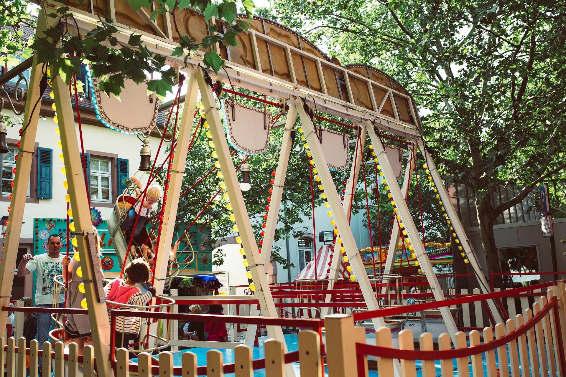 Zwei Kinder Schaukeln auf einer mit Lichter geschmückten Schiffschaukel. Die Schiffsschaukel ist sehr bunt und das Bild ist durch die Farben sehr auffregend