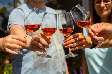 Vier Personen stoßen mit vier Stielgläsern mit Rosè Wein gefüllt an
