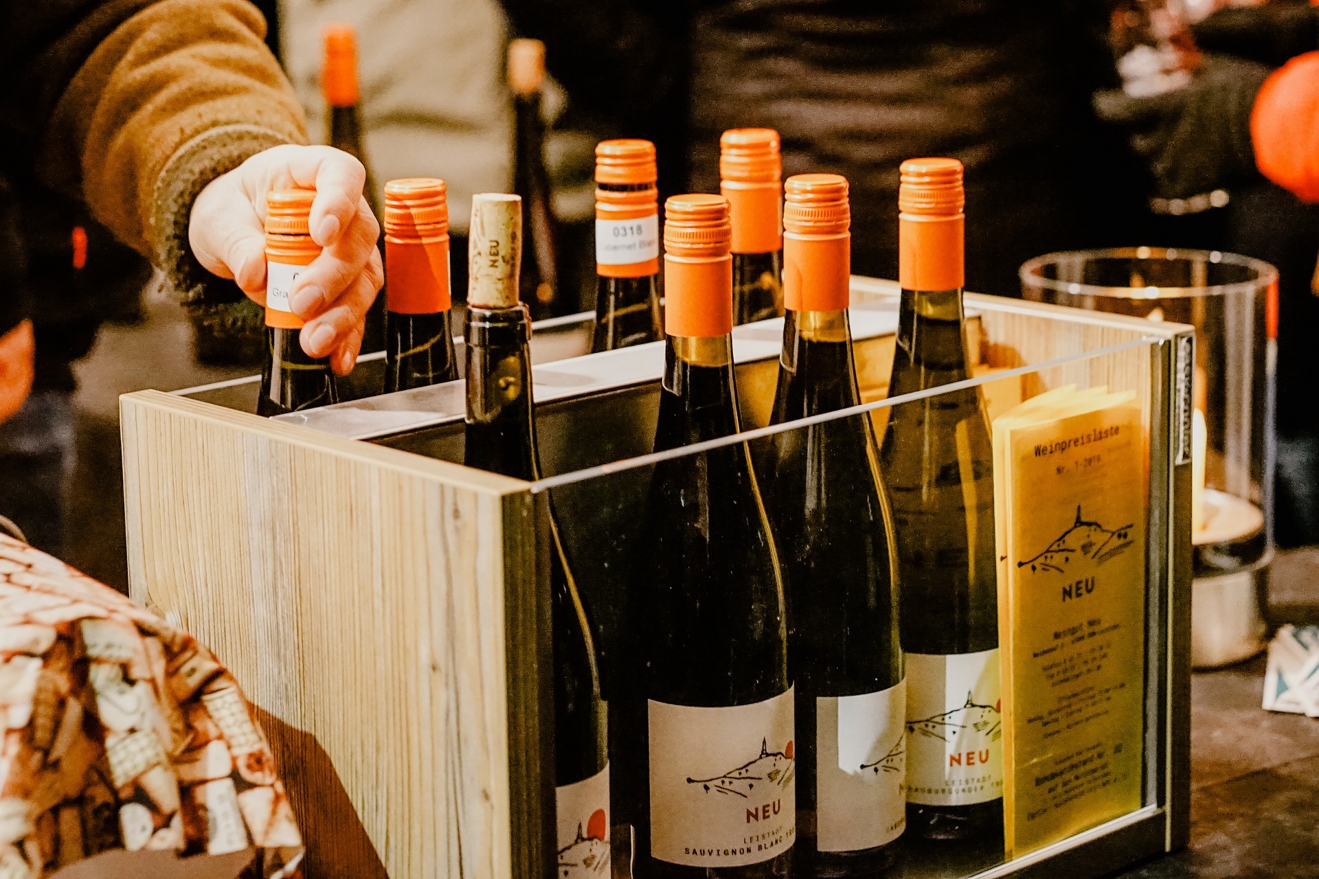 Weinausschank Weinbergnacht Weingut Neu Holzkiste mit Glasfenstern in denen die Weinflaschen des Weingut Neu lagern. Eine Hand greift nach einer Flasche.