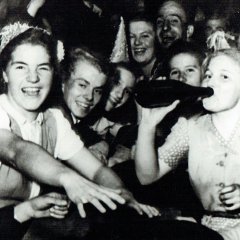 Zu sehen ist eine fröhliche Runde junger Menschen auf dem Wurstmarkt 1948, die ausgiebig feiern. Eine der Frauen trinkt aus einer Weinflasche und schaut dabei in die Kamera.