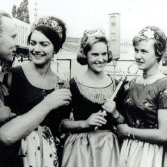 Auf dem Bild zur Wurstmarkteröffnung von 1963 sind mittig drei Damen und zu beiden Seiten jeweils ein Mann zu erkennen. Der linke Mann ist ein Kellermeister und trägt ein Küferhemd. Er prostet den Frauen und dem Mann mit einem Glas Wein zu. Bei den Frauen handelt es sich um Weinhoheiten im traditionellen Gewand und Kronen. Der rechte Mann trägt einen Anzug und Brille. Er lächelt direkt in die Kamera. 