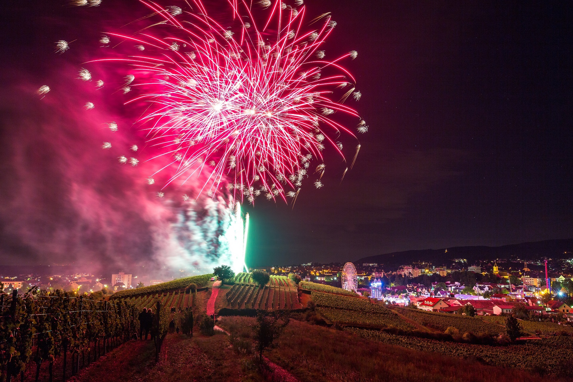 Großes Fontänenfeuerwerk oberhalb des Wurstmarktes in den Weinbergen. Der Himmel erstrahlt pink und Lila. Die Fontäne an sich erstrahlt in einem knalligen Magenta. Die Funken sind strahlend weiß.