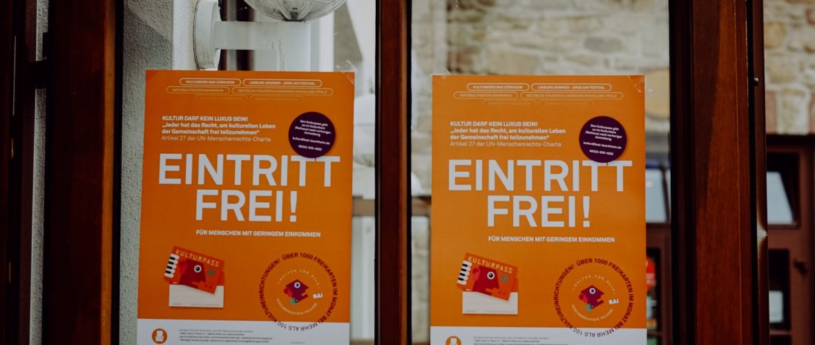 Orangene Plakate für den Kulturpass. Groß gedruckt ist zu sehen, dass der Eintritt frei ist.