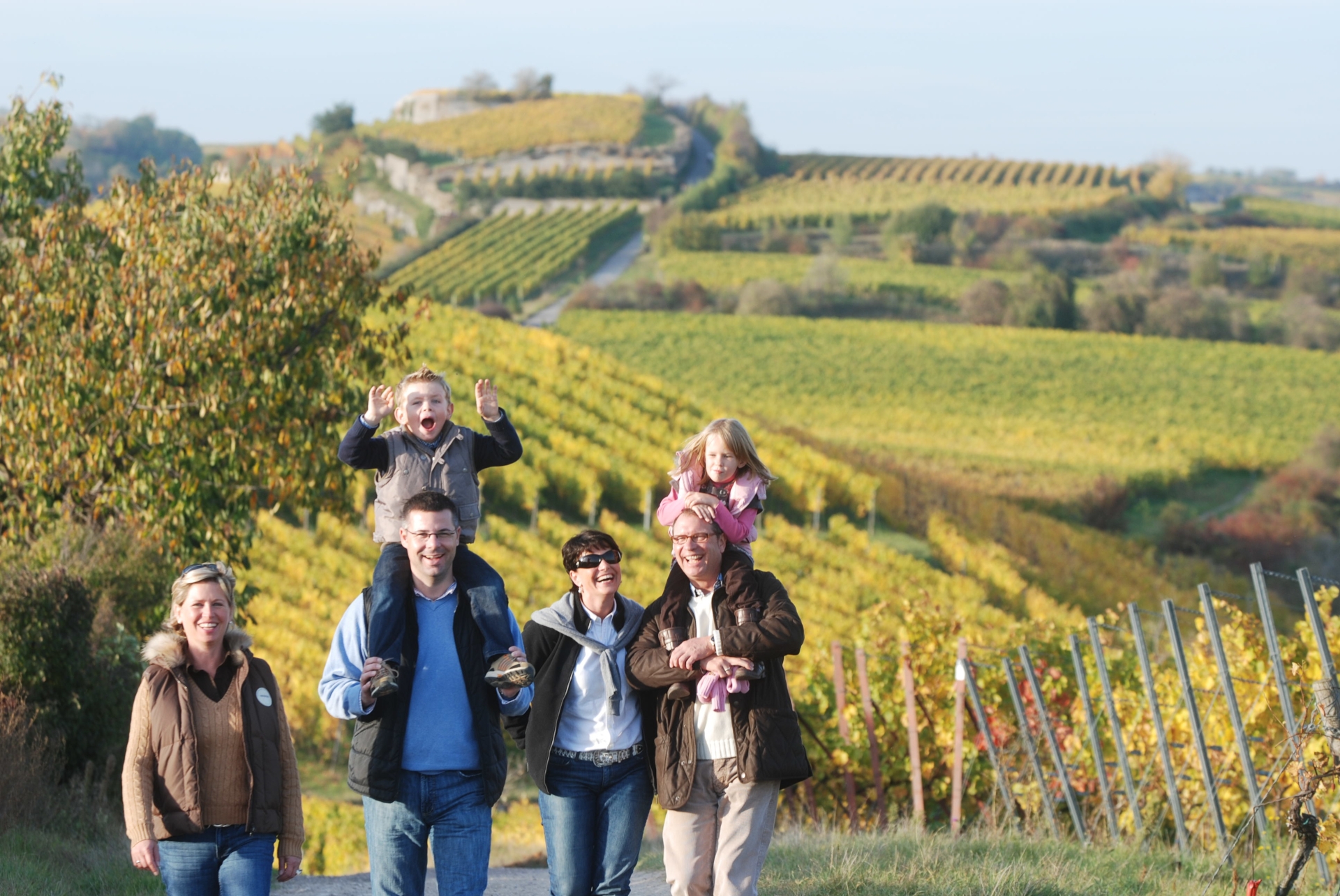 Familie in den Weinbergen Im Vordergrund wandert eine Familie. Im Hintergrund sieht man die vom Herbst verfärbten Weinberge.