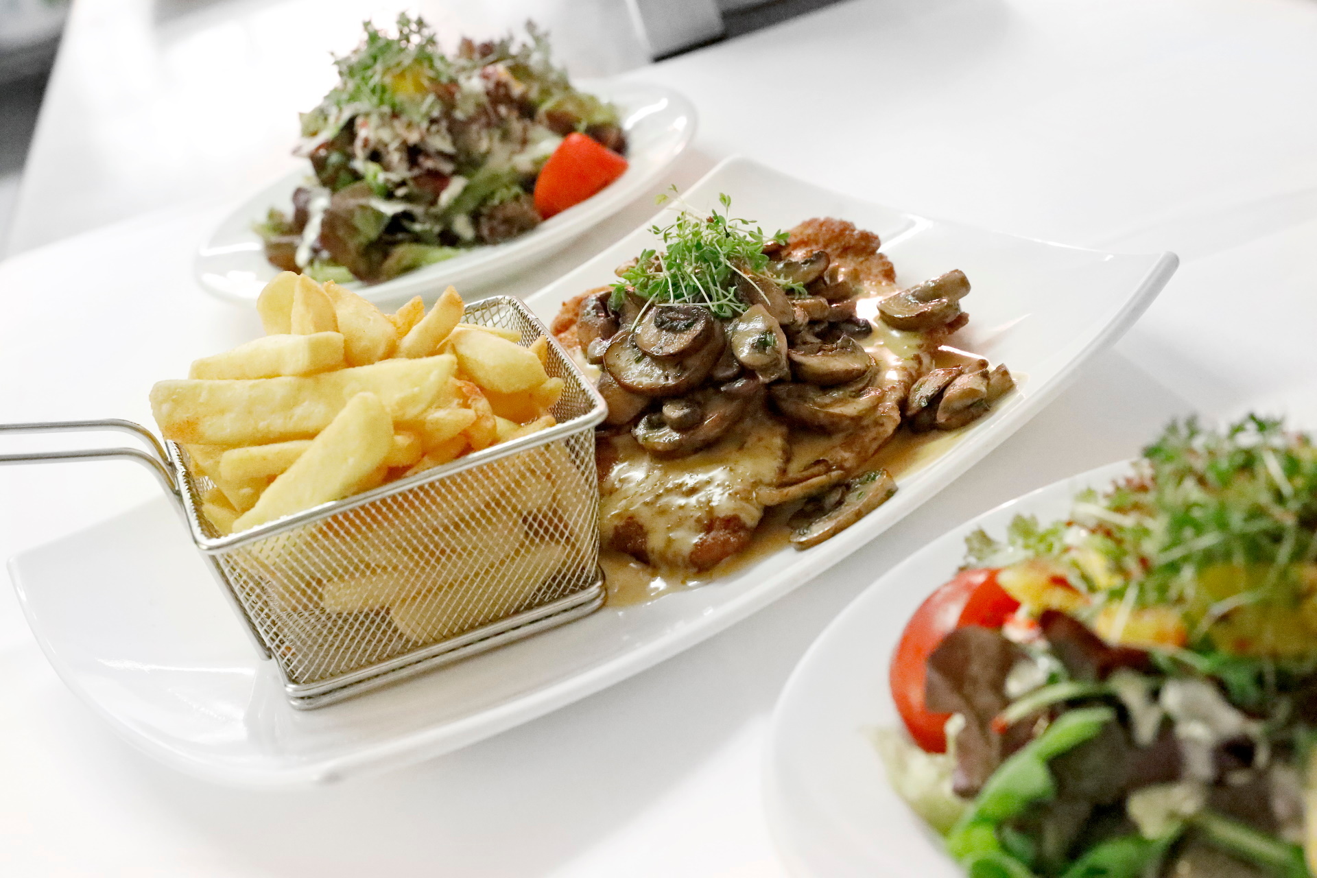 Vorne rechts der bunte Beilagensalat in der Mitte des Bildes ein Jägerschnitzel mit Pommes.