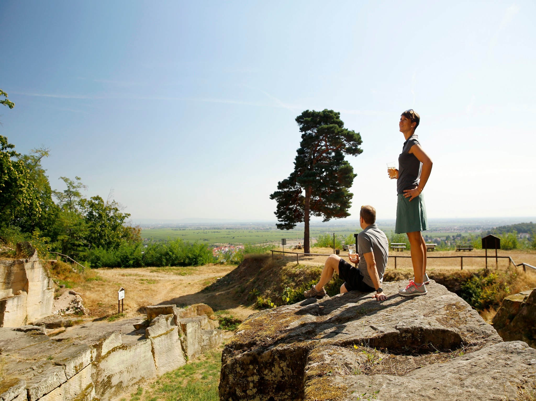 Zwei Wanderer picknicken im römischen Steinbruch Kriemhildenstuhl. Im Hintergrund der Blick nach Bad Dürkheim.