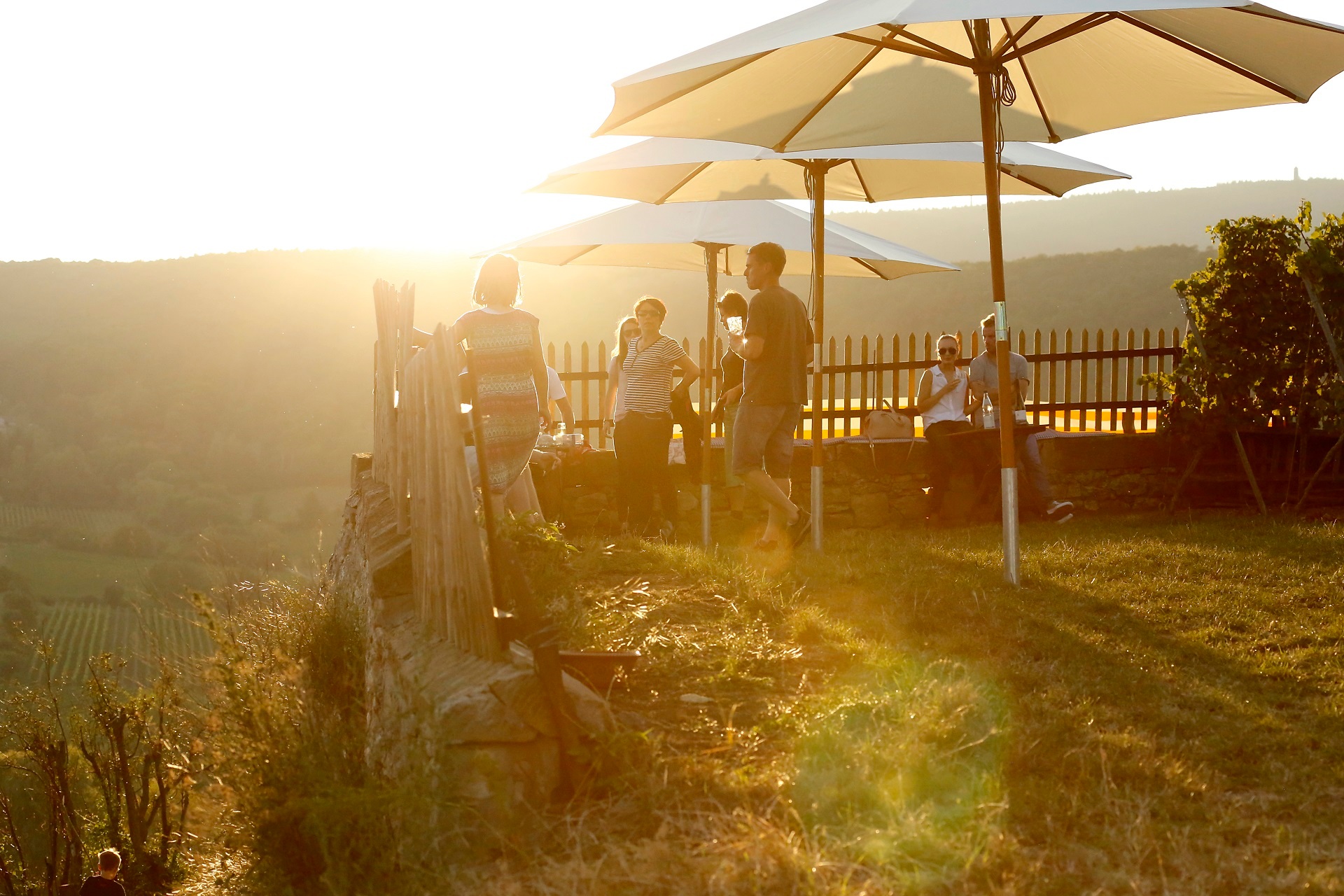 Abgebildet ist ein Ausschank auf der Römervilla Weilberg. Eine kleine Gruppen genießt ein Gläschen Wein in den letzten Sonnenstrahlen des Tages. 