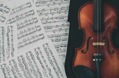 Nahaufnahme zweier Notenblätter mit einem sichtbaren Ausschnitt einer Geige am rechten Rand