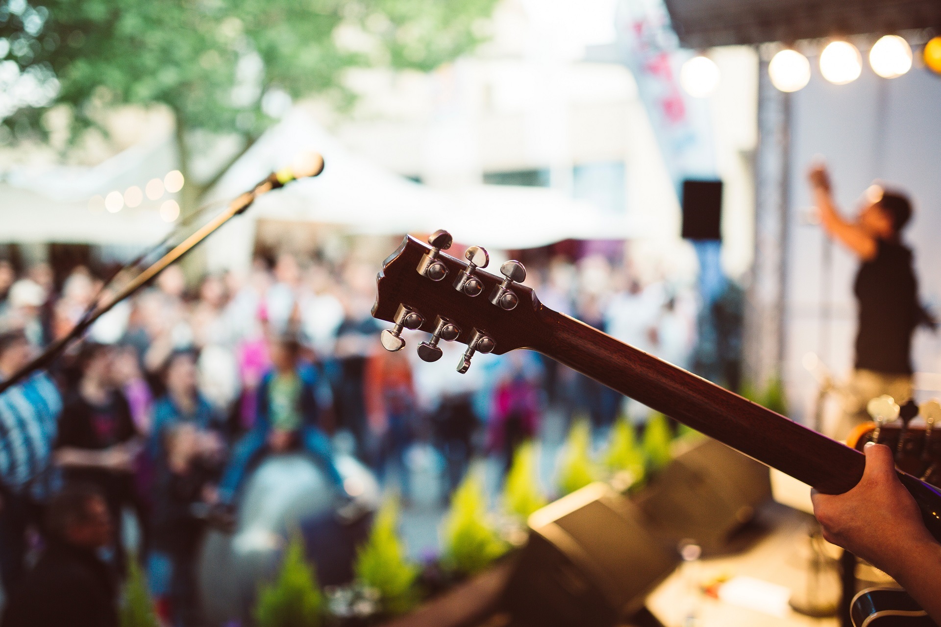Man hält Gitarre in der Hand. Publikum im Hintergrund. Feiernde Menschen.