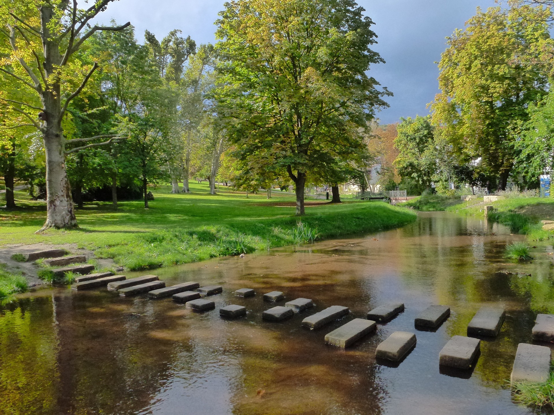 Steine in der Isenach, die einen Weg bilden über den man gehen kann. Mitten im grünen Kurpark der Stadt Bad Dürkheim.