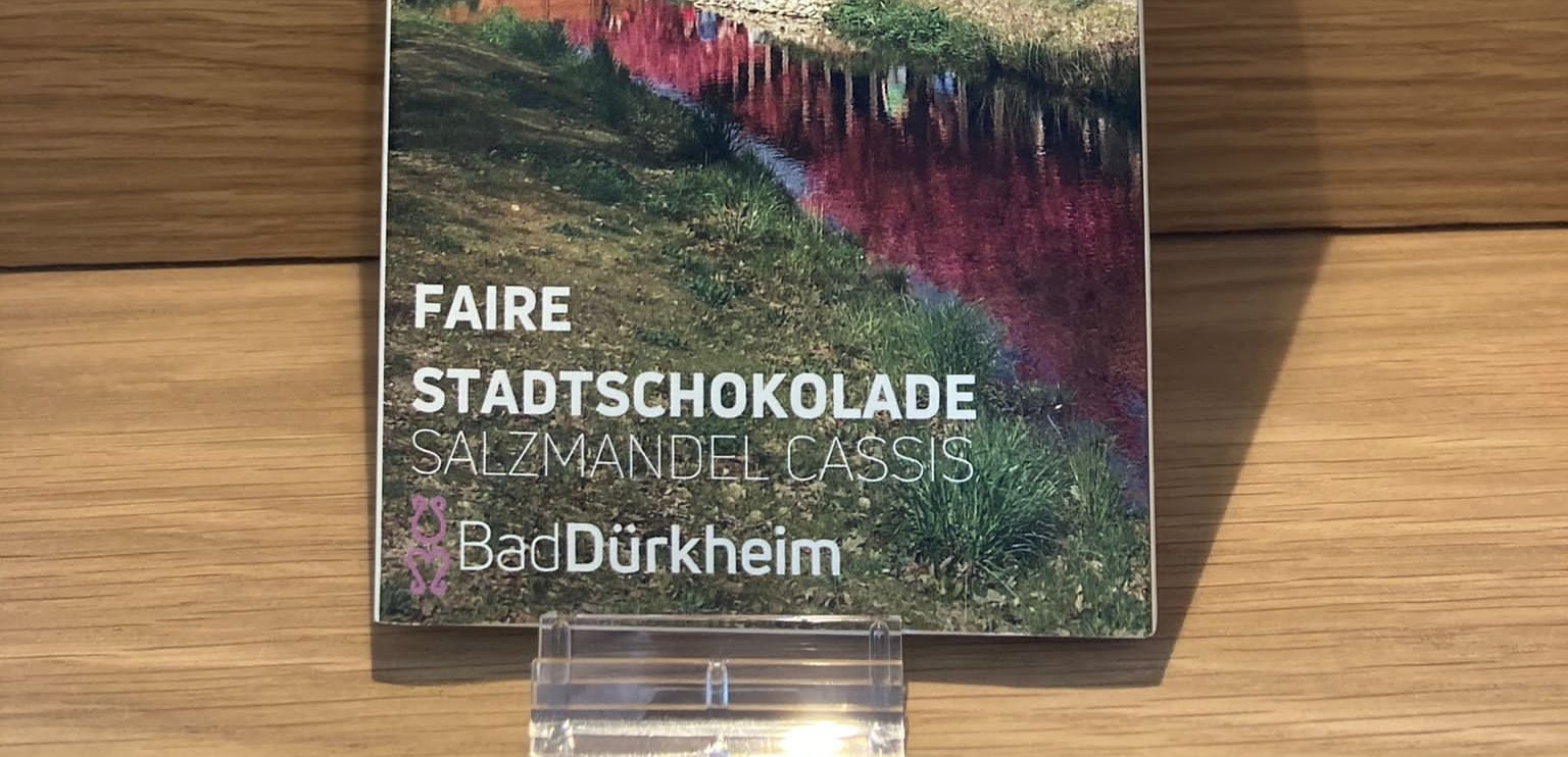 Faire Stadtschokolade Bad Dürkheim mit Salzmandel Cassis Geschmack. Vegan. Weiße Schokolade mit Salzmandel und Cassis Geschmack. Fairtrade und vegan. Verpackung mit Gradierbau-Motiv und blühenden Kirschbäumen