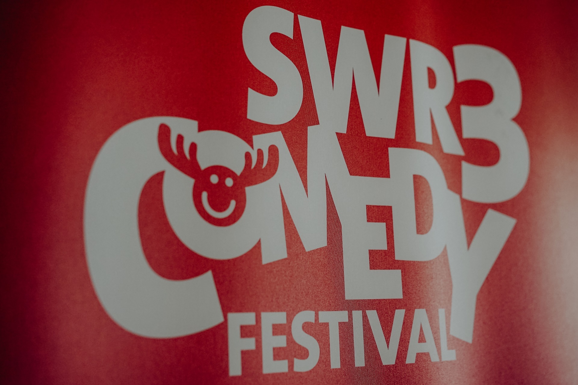 Ein weißer Schriftzug "SWR3 Comedy Festival" befindet sich auf rotem Grund. Es wurde seitlich fotografiert.