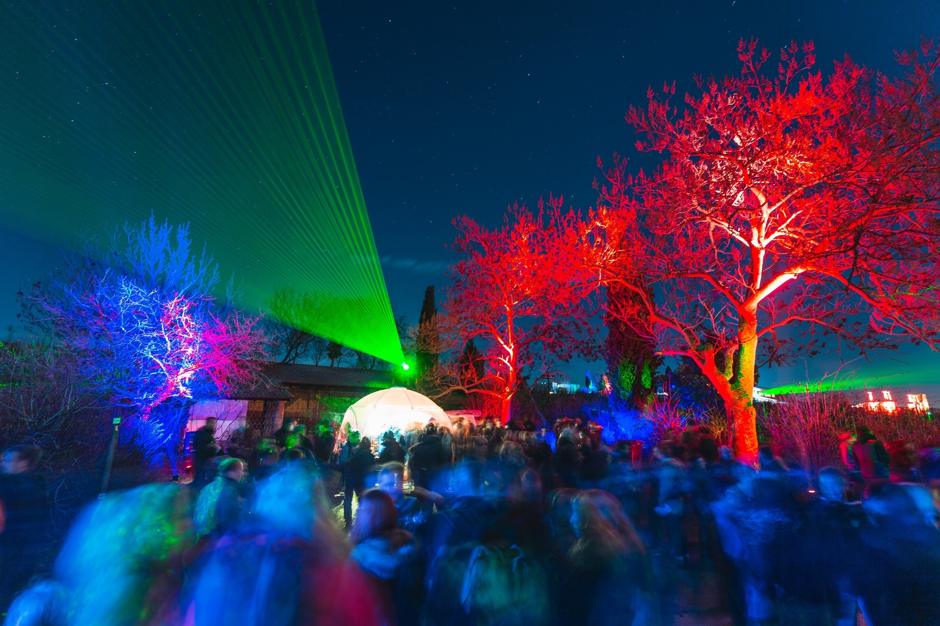 Weinbergnacht an der Römerkelter Die Römerkelter bei Nacht, mit einem grünen Fächerlaser, links im Bild ist ein blau beleuchteter Baum zu sehen, auf der rechten Seite sind zwei rot angestrahlte Bäume zu sehen. Im Vordergrund sind viele Besucher der Bad Dürkheimer Weinbergnacht verschwommen zu erkennen