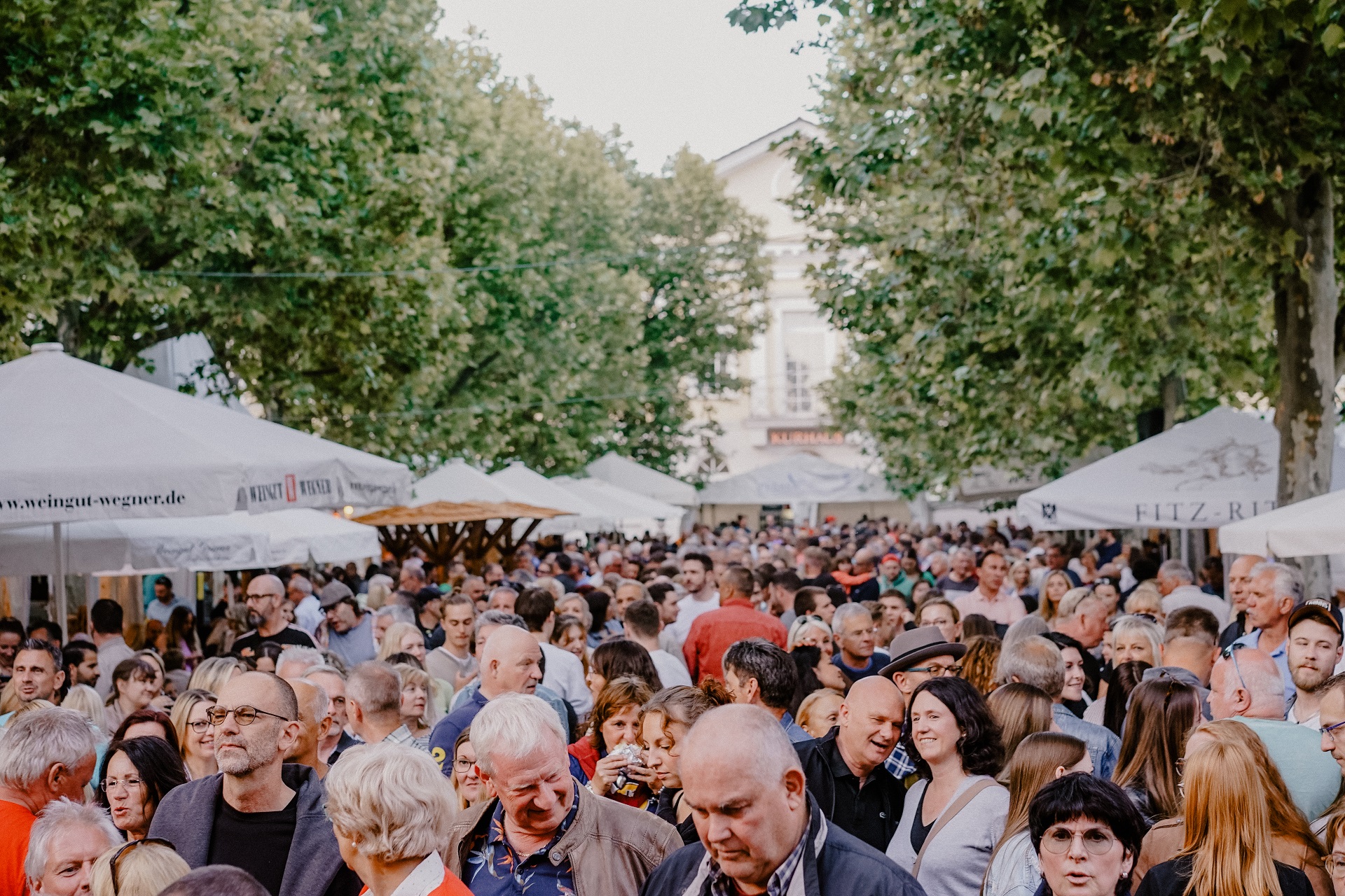 Im Hintergrund sieht man verschwommen das Kurparkhotel. Davor tummeln sich hunderte Besucher zwischen den Ausschankstellen. Zu sehen sind nur die Schultern und die Köpfe der Stadtfest Besucher.