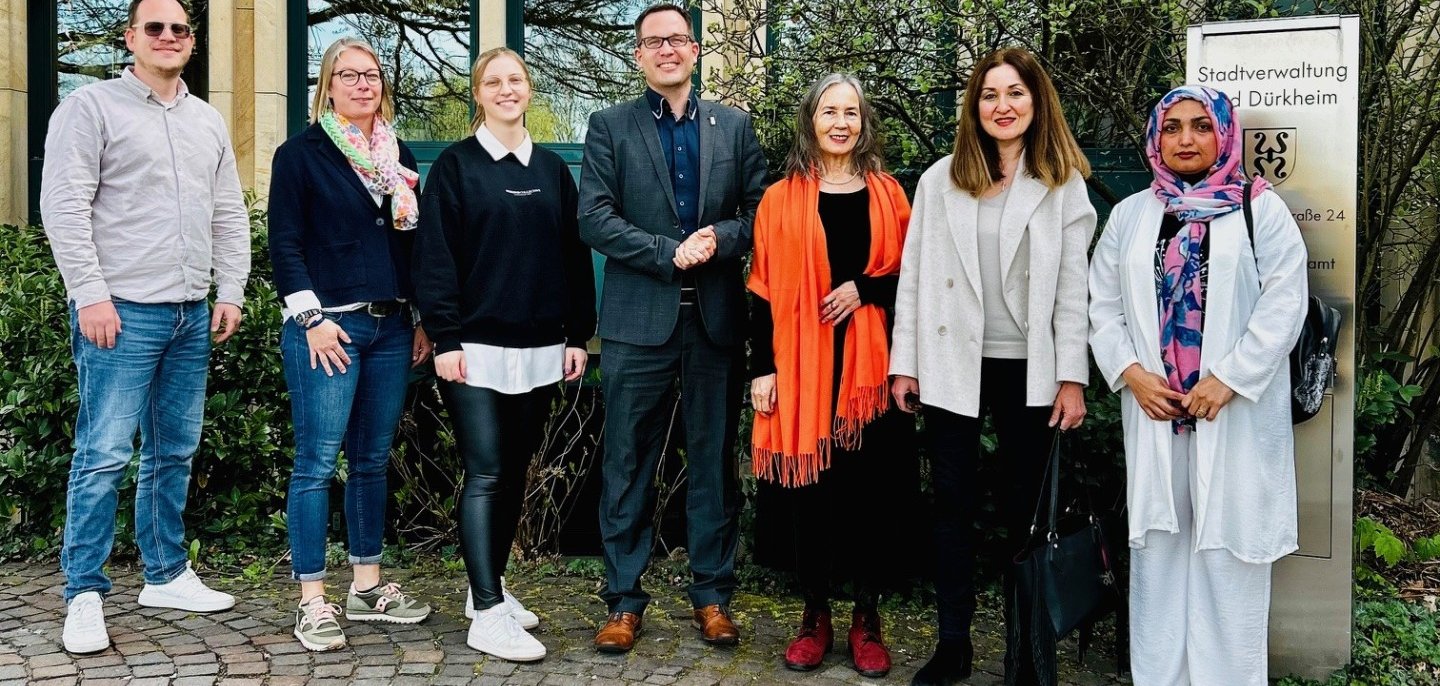 Vertreter und Vertreterinnen der Stadt Bad Dürkheim und dem Beirat für Migration treffen sich zu einem ersten gemeinsamen Treffen. Sie posieren für ein Foto vor der Tür der Stadtverwaltung.