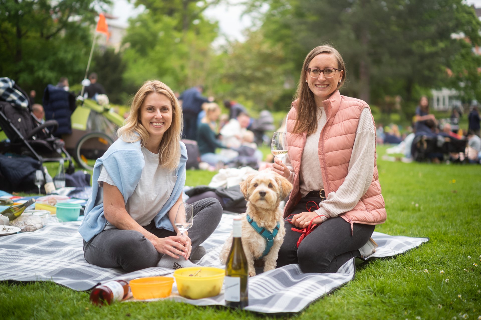 Zwei Frauen sitzen auf einer Picknickdecke im Park mit Hund während des Winzerpicknicks im Bad Dürkheimer Kurpark.