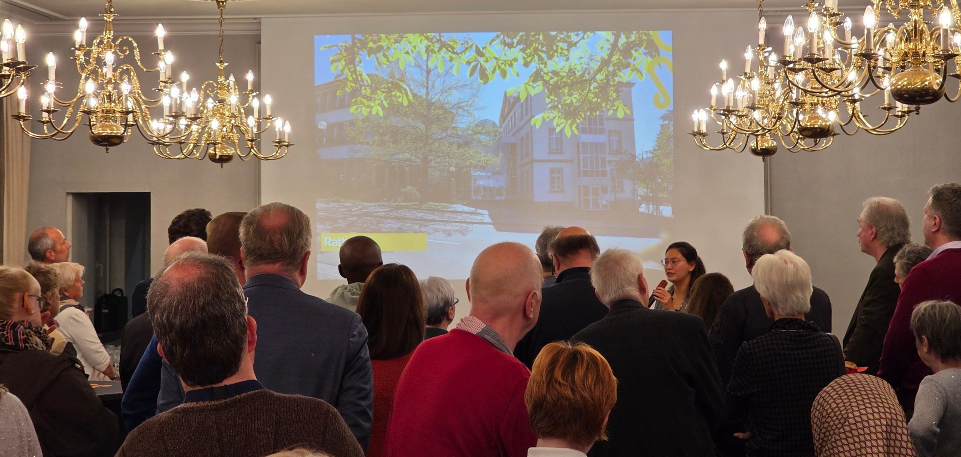 Menschenmenge mit Bürgermeisterin vor einer Beamer Leinwand