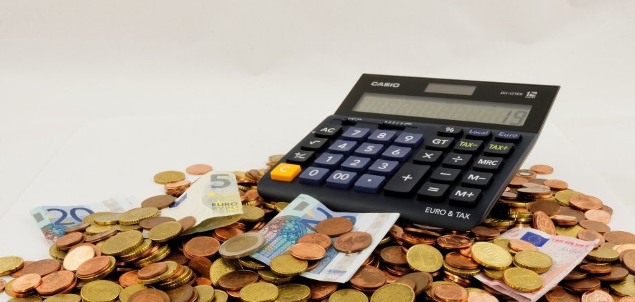 Taschenrechner liegt auf Münzgeldhaufen und daneben liegen Geldscheine