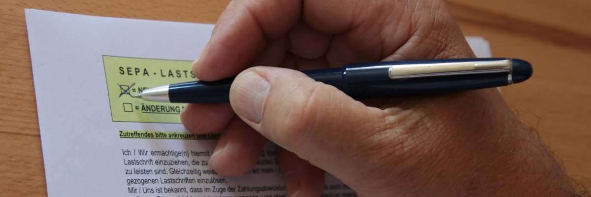 Hand mit Stift. Person füllt gerade das SEPA Lastschriftmandat aus